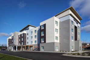 A multi-story hotel with a modern design, featuring a covered entrance area with outdoor seating. - TownePlace Suites by Marriott Grand Rapids Airport (Grand Rapids)