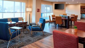 A hotel lobby with seating areas, a flat-screen TV, and a bookshelf. - TownePlace Suites by Marriott Grand Rapids Airport (Grand Rapids)