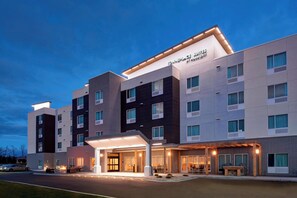 A modern hotel with a flat roof, multiple floors, and a well-lit entrance. - TownePlace Suites by Marriott Grand Rapids Airport (Grand Rapids)