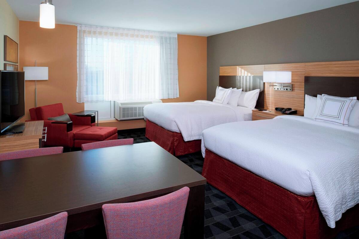 A hotel room with two beds, a desk, a chair, a TV, and a window with curtains.