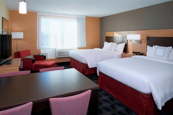 A hotel room with two beds, a desk, a chair, a TV, and a window with curtains.