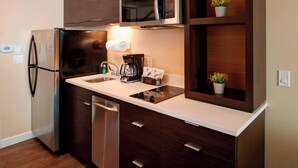 A compact kitchen with a stainless steel refrigerator, a built-in microwave, a coffee maker, and a dishwasher. - TownePlace Suites by Marriott Grand Rapids Airport (Grand Rapids)