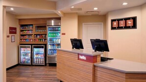 A reception area with a counter, two monitors, a refrigerator stocked with beverages, and a vending machine. - TownePlace Suites by Marriott Grand Rapids Airport (Grand Rapids)