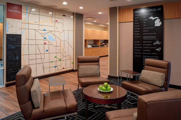 A hotel lobby with leather seating, a map on the wall, and a sign detailing Grand Rapids, MI. - TownePlace Suites by Marriott Grand Rapids Airport (Grand Rapids)