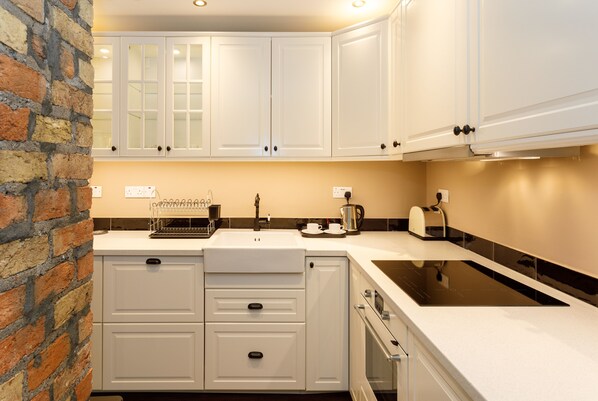 A kitchen with white cabinets, a brick wall, a black stove, and a coffee maker. - Molloy's Apartments (Dublin)