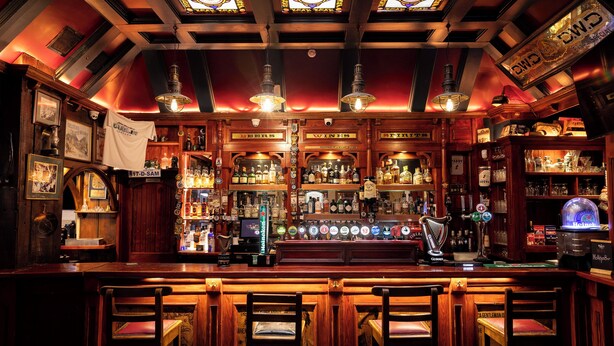Un bar con mobiliario de madera, una variedad de botellas y una selección de cervezas.