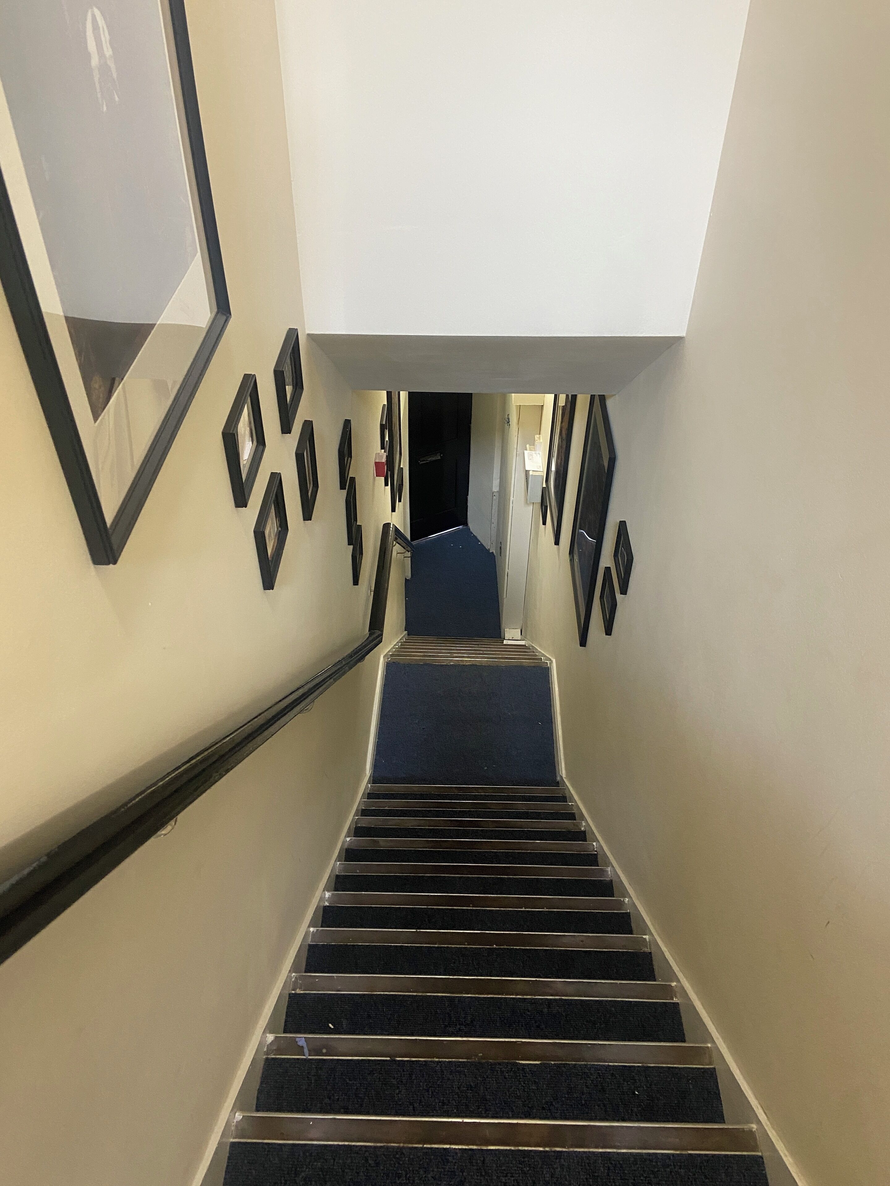 Un escalier avec un palier recouvert de moquette et des murs ornés de tableaux encadrés.
