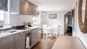 Una cocina moderna con armarios grises, encimera blanca y zona de comedor con sillas y mesa blancos.
