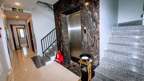 A hotel lobby with a marble staircase, an elevator, and a fire extinguisher. - My Family (Da Nang)