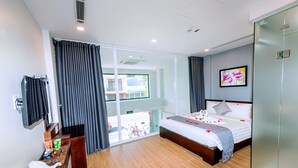 A hotel room with a bed, a desk, a chair, a television, and a view of the outside. - My Family (Da Nang)
