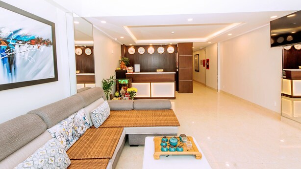 A modern hotel lobby with a sofa, a coffee table, and a reception desk. - My Family (Da Nang)