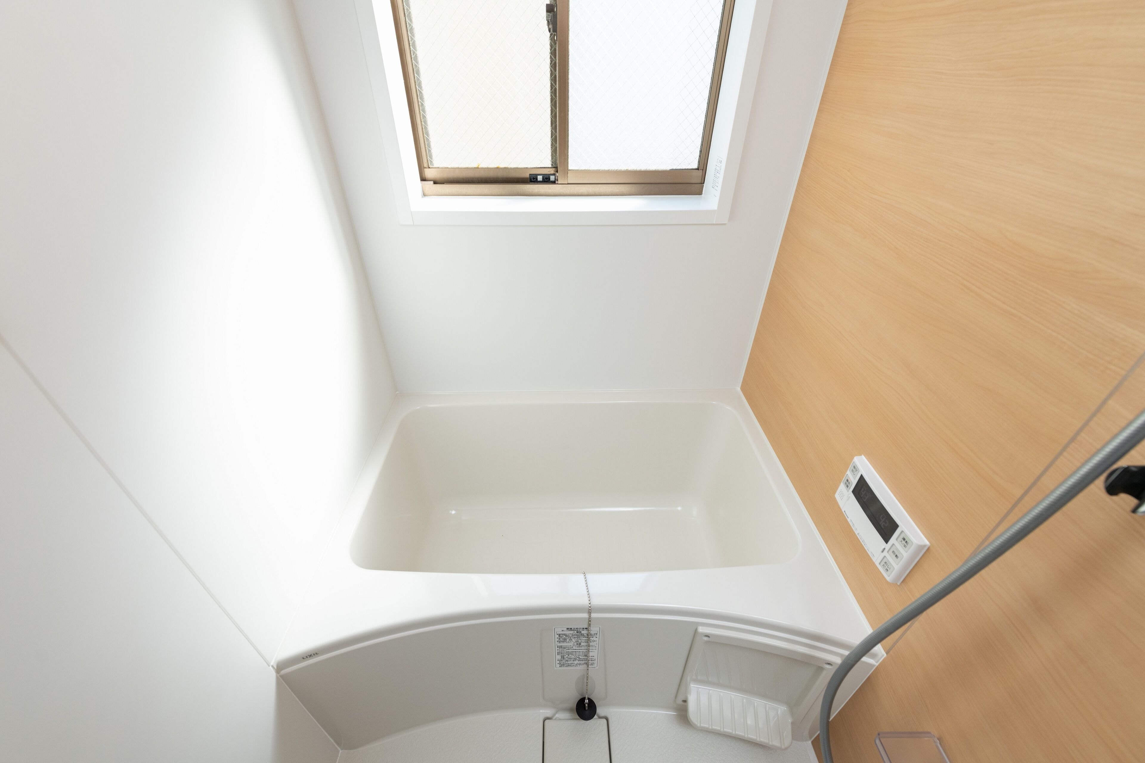 A bathroom with a white bathtub, a window, and a control panel.