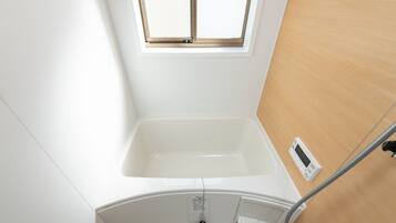 A bathroom with a white bathtub, a window, and a control panel.