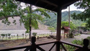 Un espacio al aire libre techado con vistas a un río y colinas. Se observa una pequeña construcción con techo y una señal.