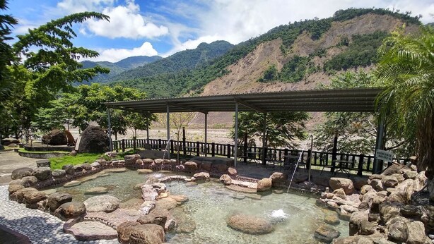 Un área de aguas termales con un sendero de piedra, rocas y una estructura de madera.