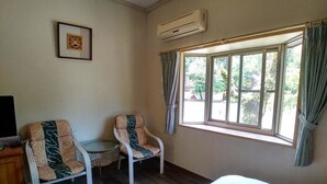 Habitación de hotel con cama, dos sillones, una mesita, televisión y ventana con cortinas.