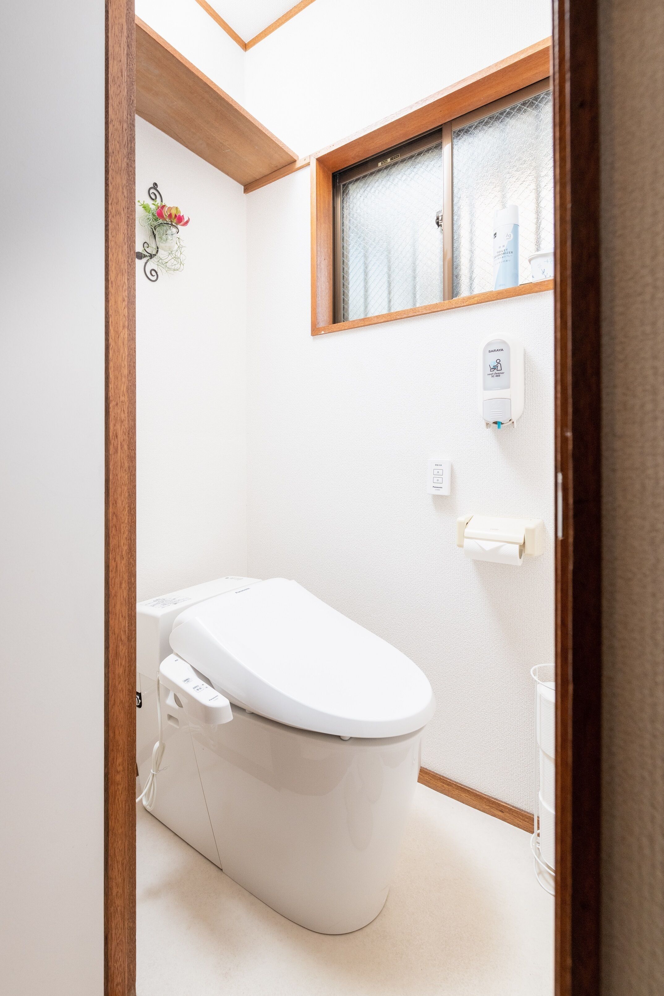 Un baño pequeño y moderno con inodoro, ventana y dispensador de gel antibacterial.