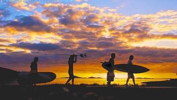 Ein Sonnenuntergang mit Silhouetten von Personen, die Surfbretter tragen.