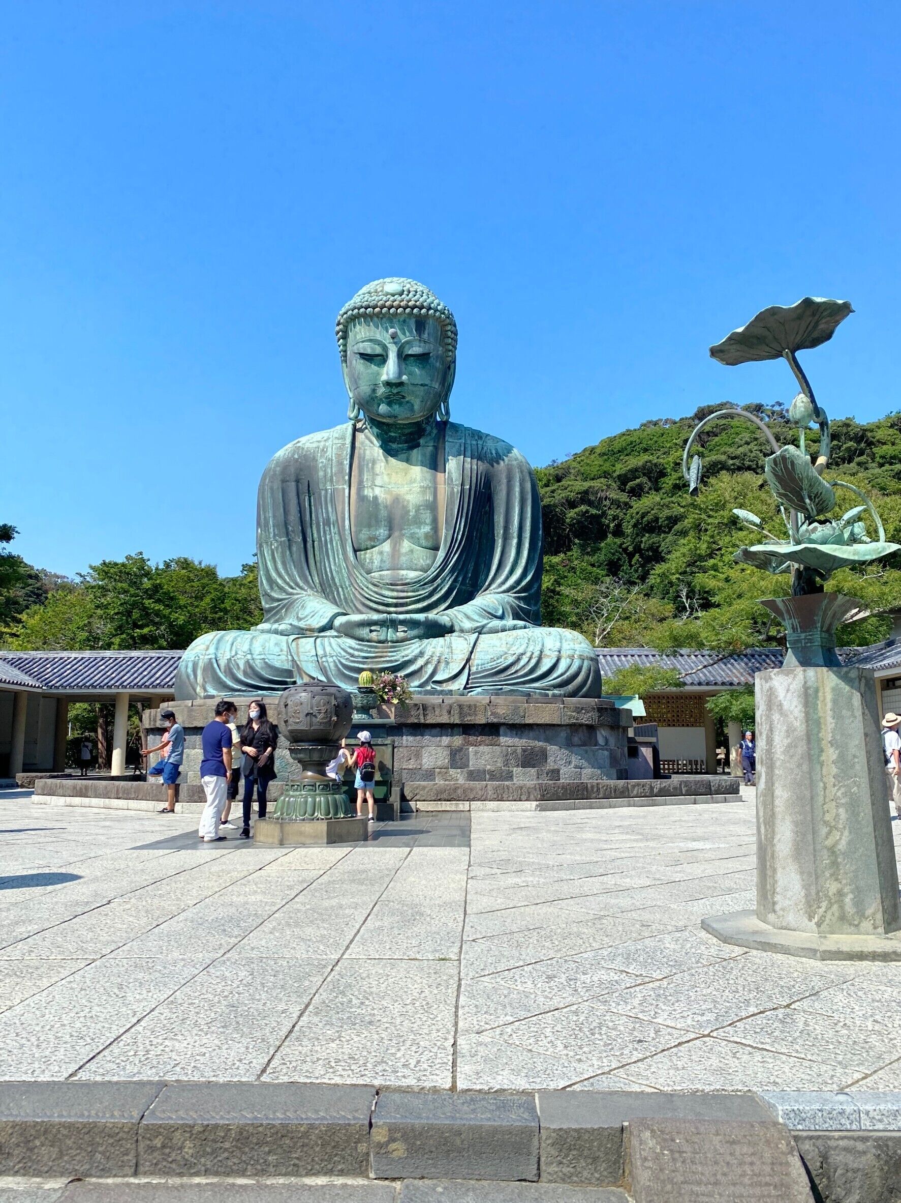 Eine große Buddha-Statue in einem Innenhof mit einem traditionellen Gebäude im Hintergrund.