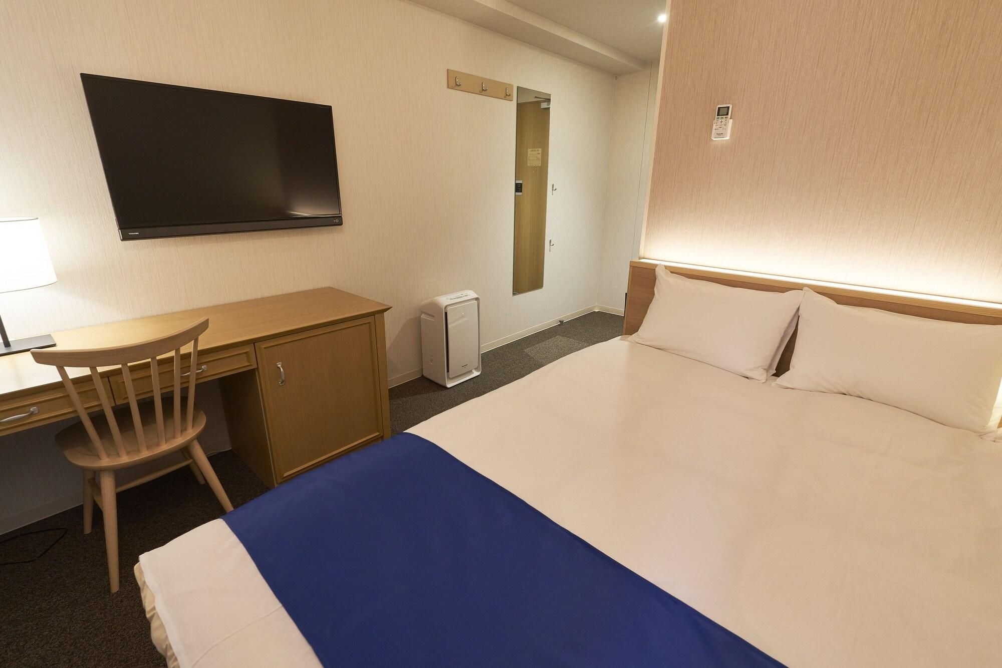 A hotel room with a bed, a desk, a chair, a television, and a heater.