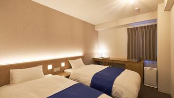Ein Hotelzimmer mit zwei Betten, einem Schreibtisch, einem Stuhl, einer Lampe und einem Vorhangfenster.