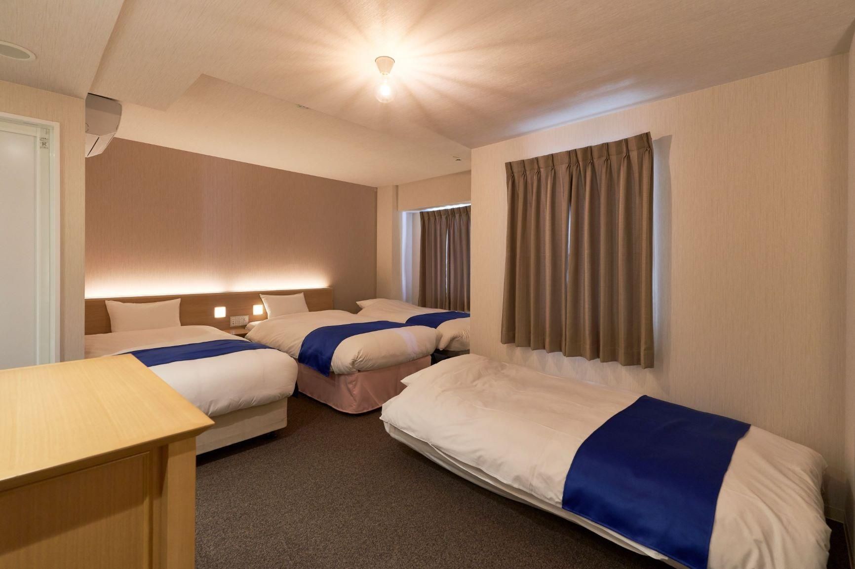 Habitación de hotel con dos camas, un escritorio y una ventana con cortinas.