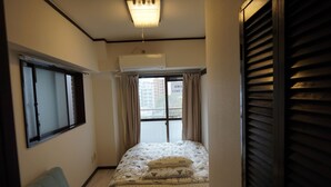Ein Schlafzimmer mit Bett, Stuhl, Fenster mit Vorhängen und Klimaanlage.