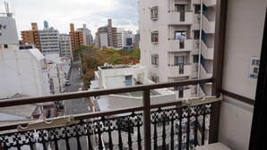 Blick von einem Balkon mit Metallgeländer auf ein Stadtbild mit verschiedenen Gebäuden, darunter Wohn- und Geschäftsgebäuden.
