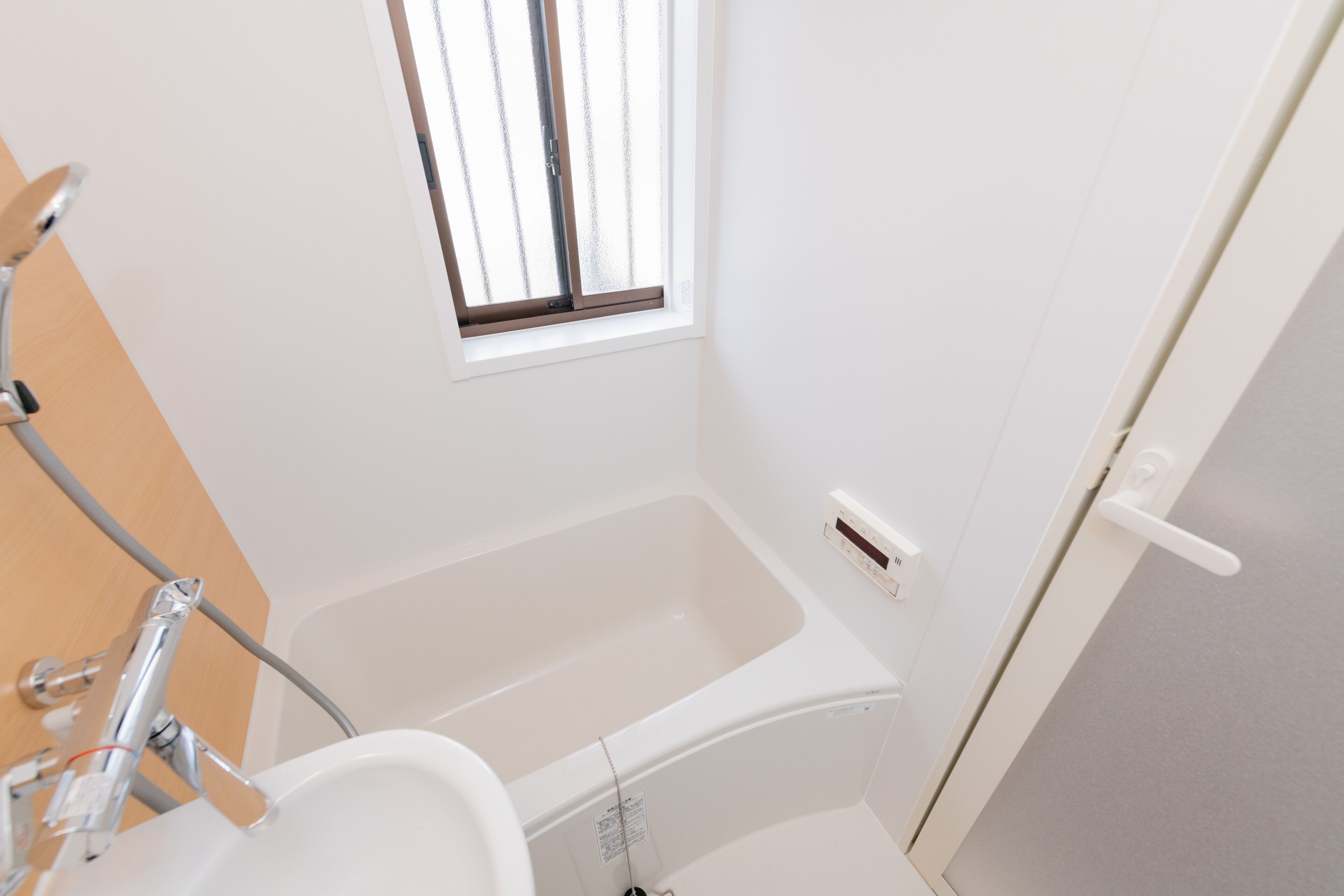 A small, clean bathroom with a bathtub, a window, and a shower area.