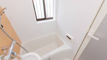 A small, clean bathroom with a bathtub, a window, and a shower area.