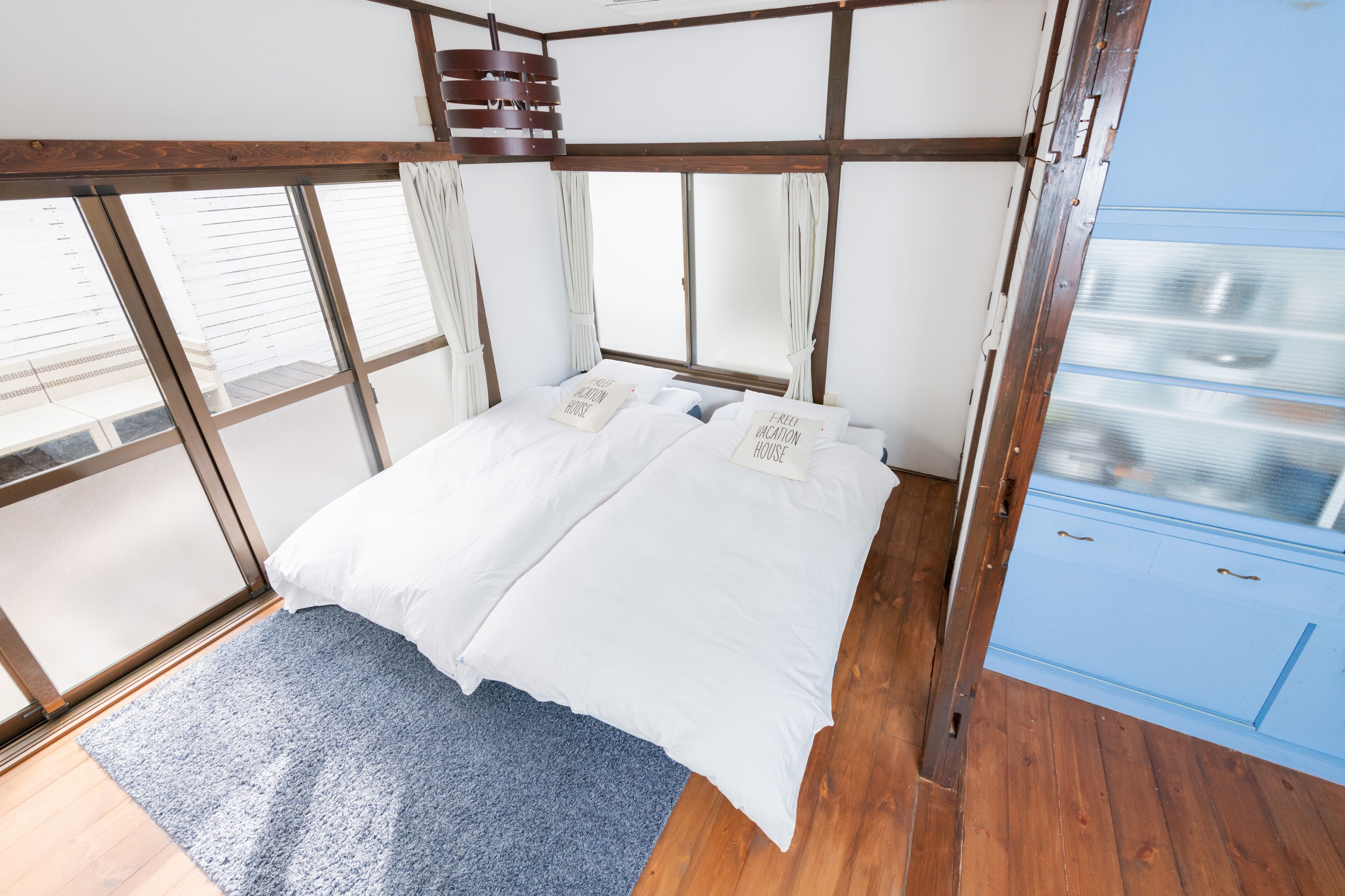A bedroom with a wooden ceiling, a bed with white bedding, a blue carpet, and a window with curtains.