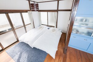 A bedroom with a wooden ceiling, a bed with white bedding, a blue carpet, and a window with curtains.
