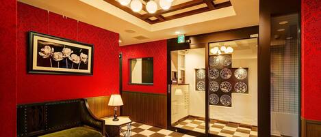 A lobby with a checkered floor, a green sofa, a framed picture of flowers, and a wall with circular patterns.