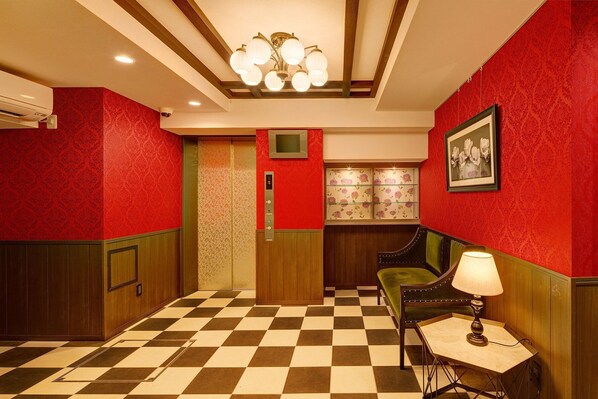 Un vestíbulo de hotel con piso a cuadros, paredes de diseño rojo y un banco tapizado en verde, además de una mesa con lámpara.