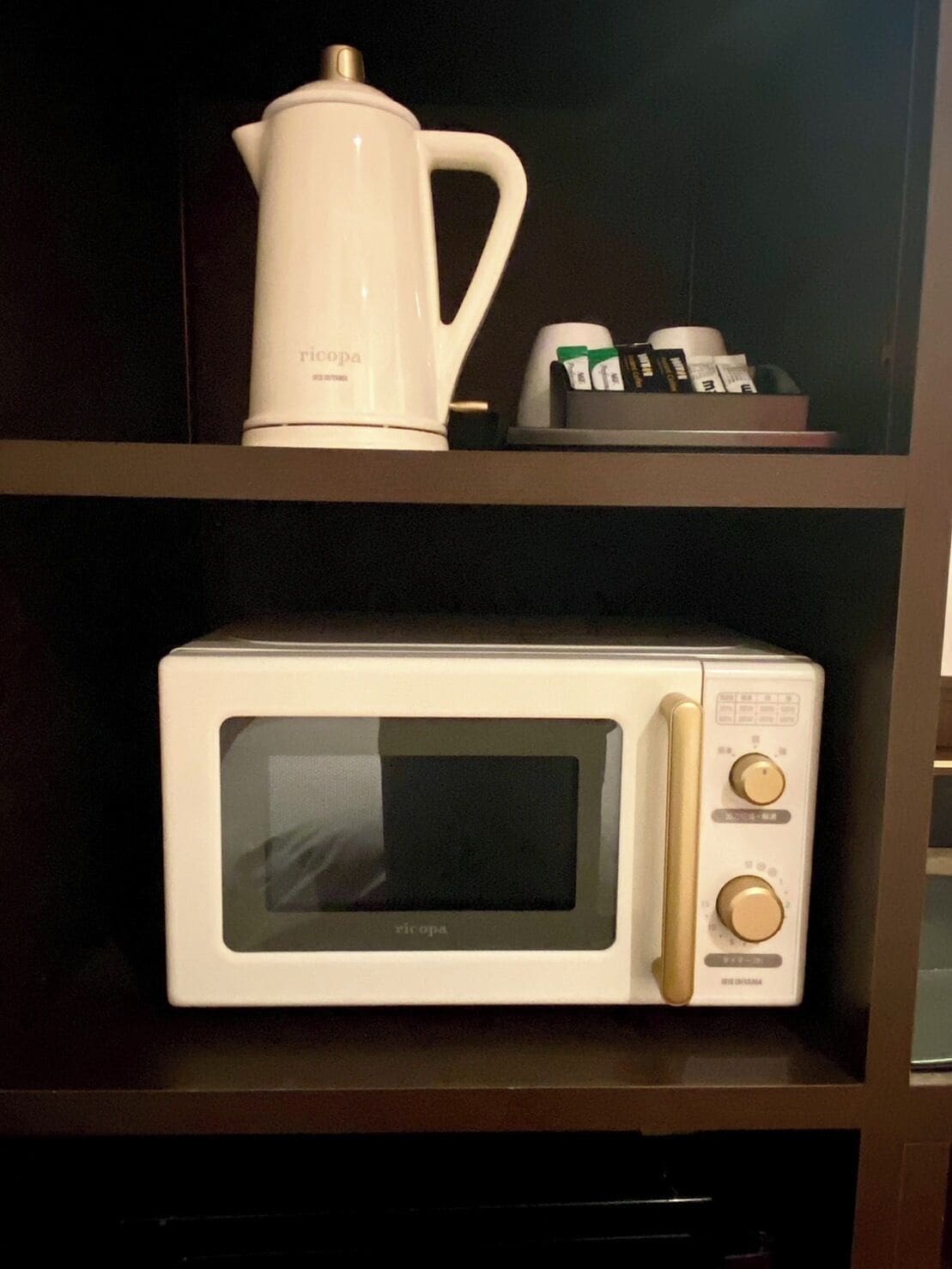 Un horno microondas en un estante con una cafetera y una caja de cápsulas de café.