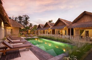 A resort with thatched-roof bungalows, a swimming pool, and lounge chairs. - Nusa Majesty (Penida Island)