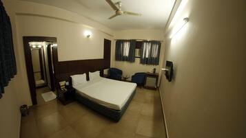 A hotel room with a large bed, a ceiling fan, a desk with a chair, and a small table with a lamp.