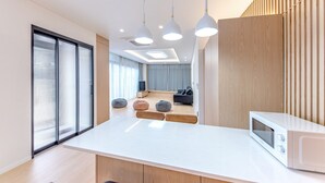 Een moderne keuken met een wit aanrecht, een magnetron, hanglampen en een schuifdeur naar een woonruimte.