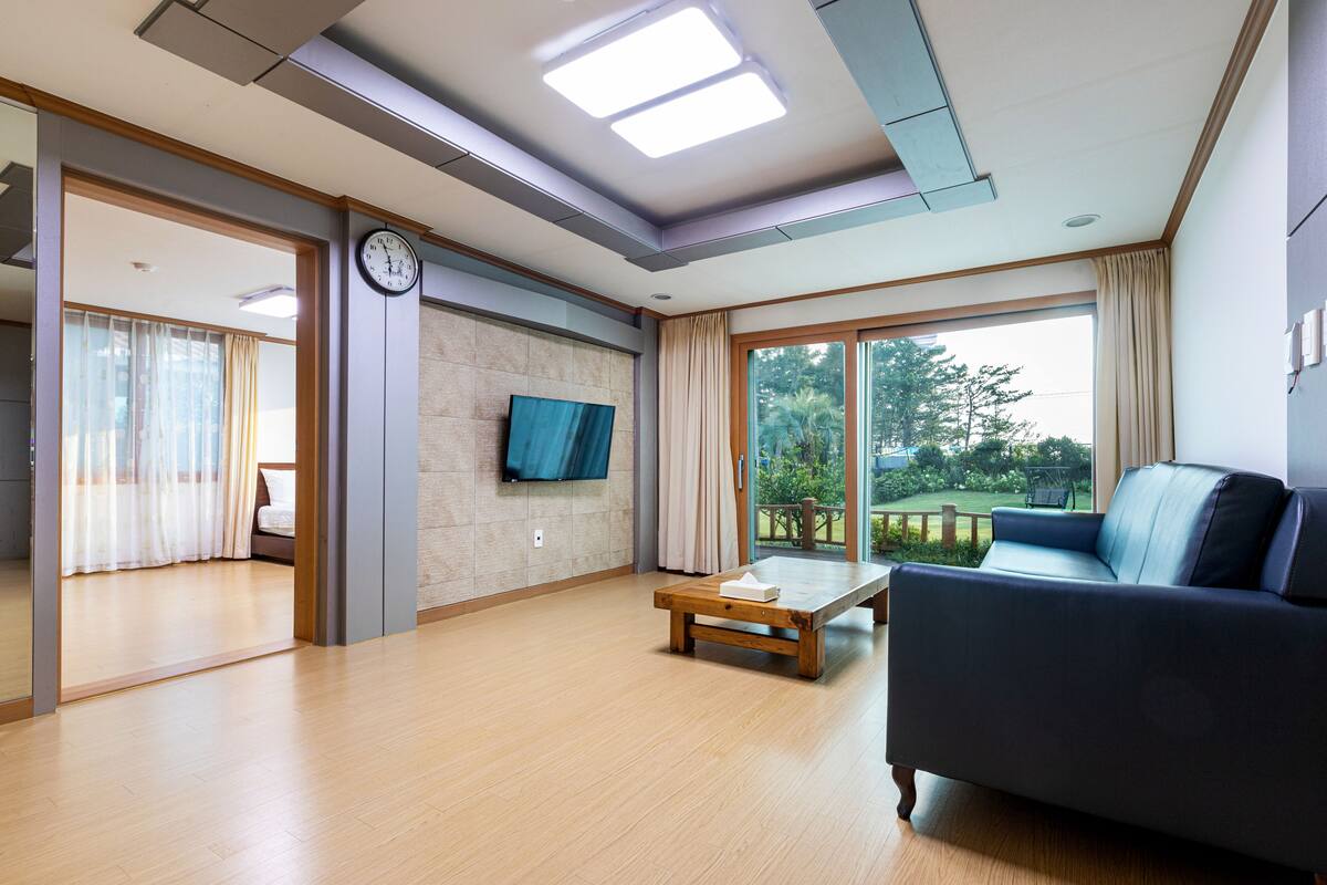 Un salón amplio con un ventanal grande, un sofá, una mesa de centro de madera y un televisor de pantalla plana montado en la pared.