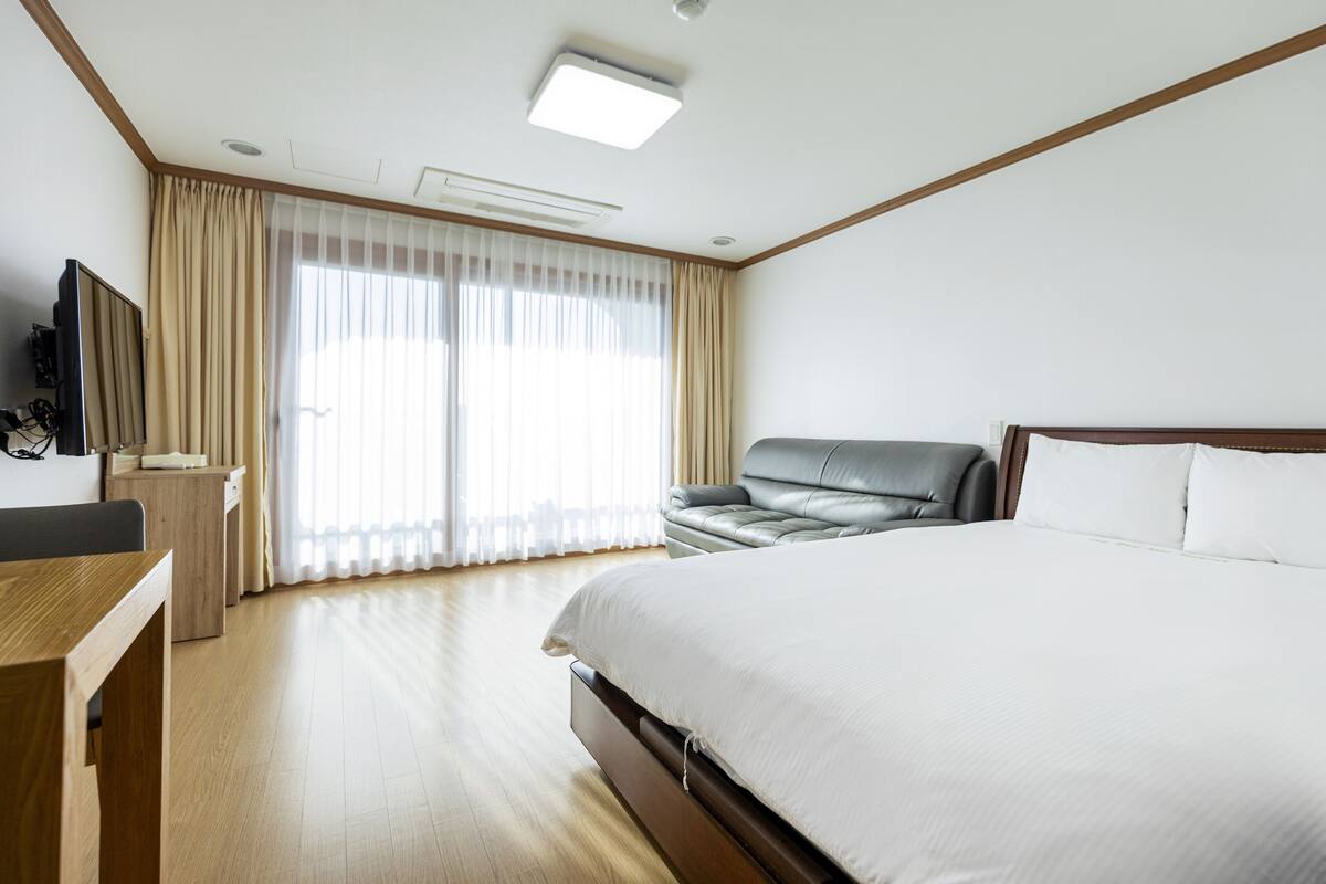 Una habitación de hotel con una cama grande, un escritorio, un sofá de cuero y un televisor.