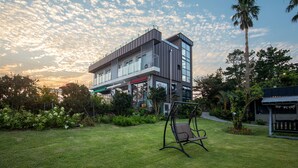 Een modern gebouw met een plat dak, grote ramen en een schommelstoel in de tuin.
