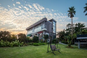 Un edificio moderno con techo plano, ventanas grandes y una mecedora en el jardín.
