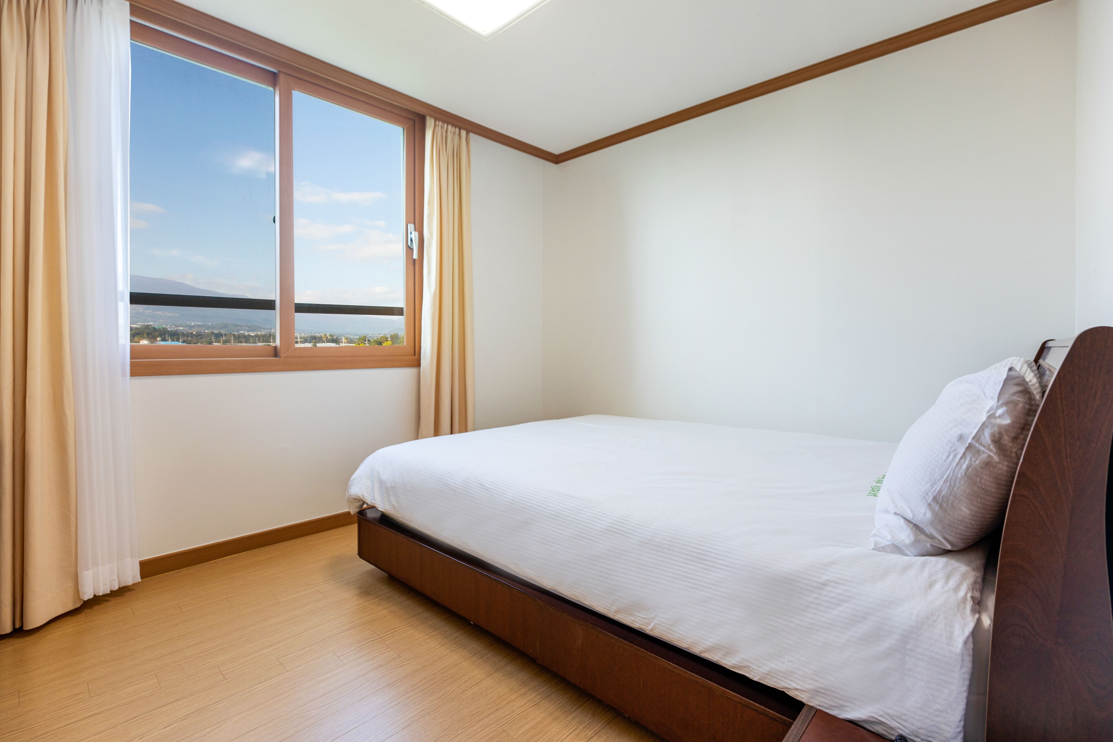A bedroom with a single bed, a large window with curtains, and a view of a body of water.