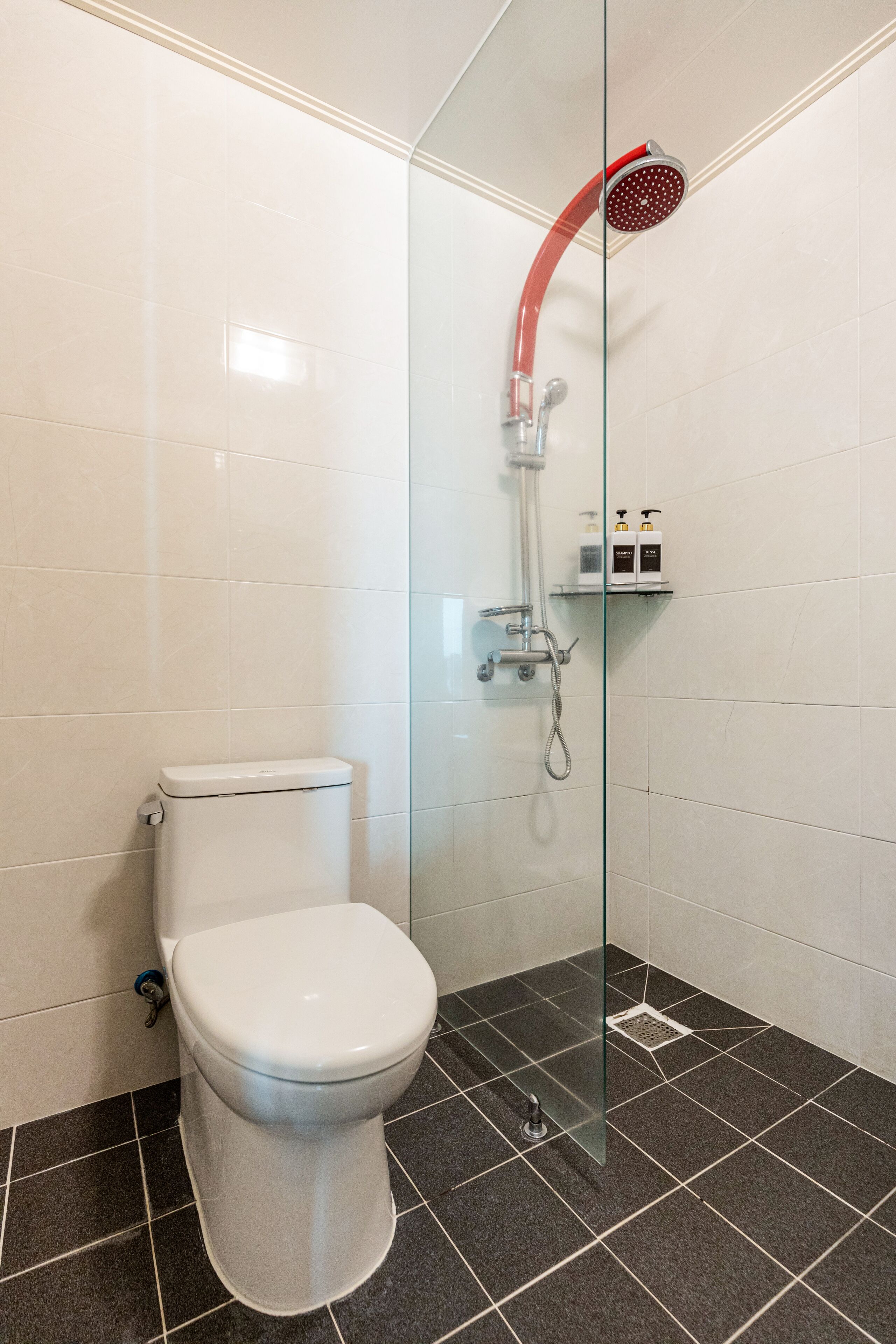 A modern bathroom with a glass-enclosed shower, a white toilet, and a black tiled floor.