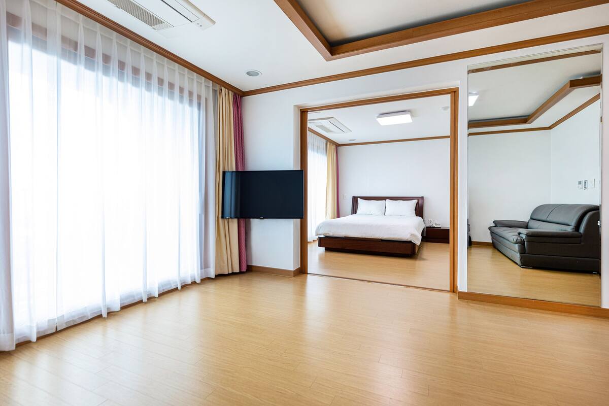 Una habitación de hotel moderna con piso de madera, una cama grande, un televisor de pantalla plana y un sofá.