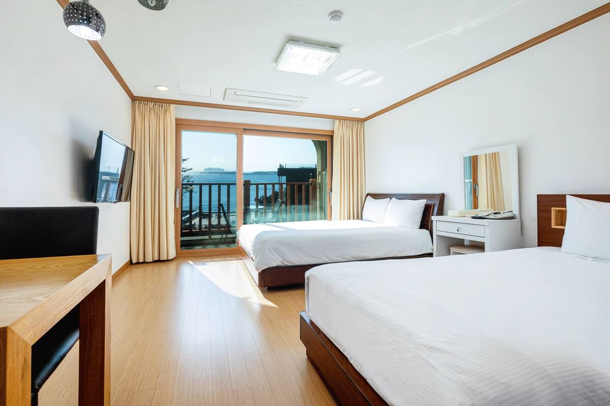 Habitación de hotel con dos camas, un escritorio, un televisor y un balcón con vistas al mar.