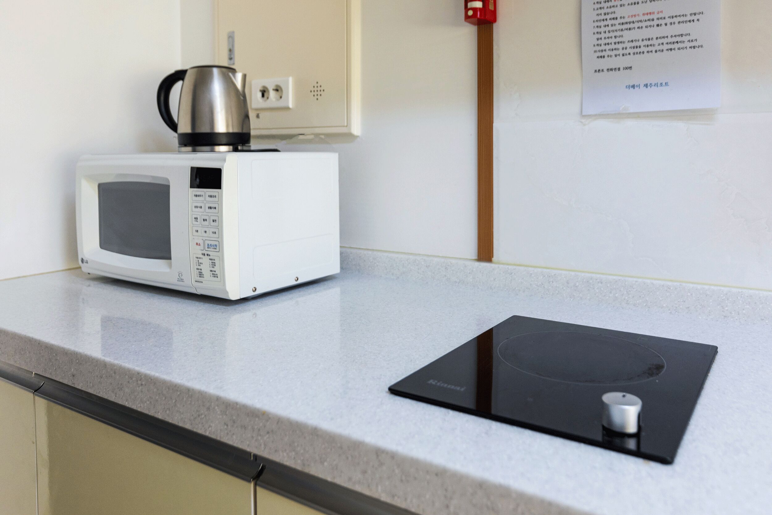 A kitchen with a microwave, a kettle, and a black induction cooktop on a granite countertop.