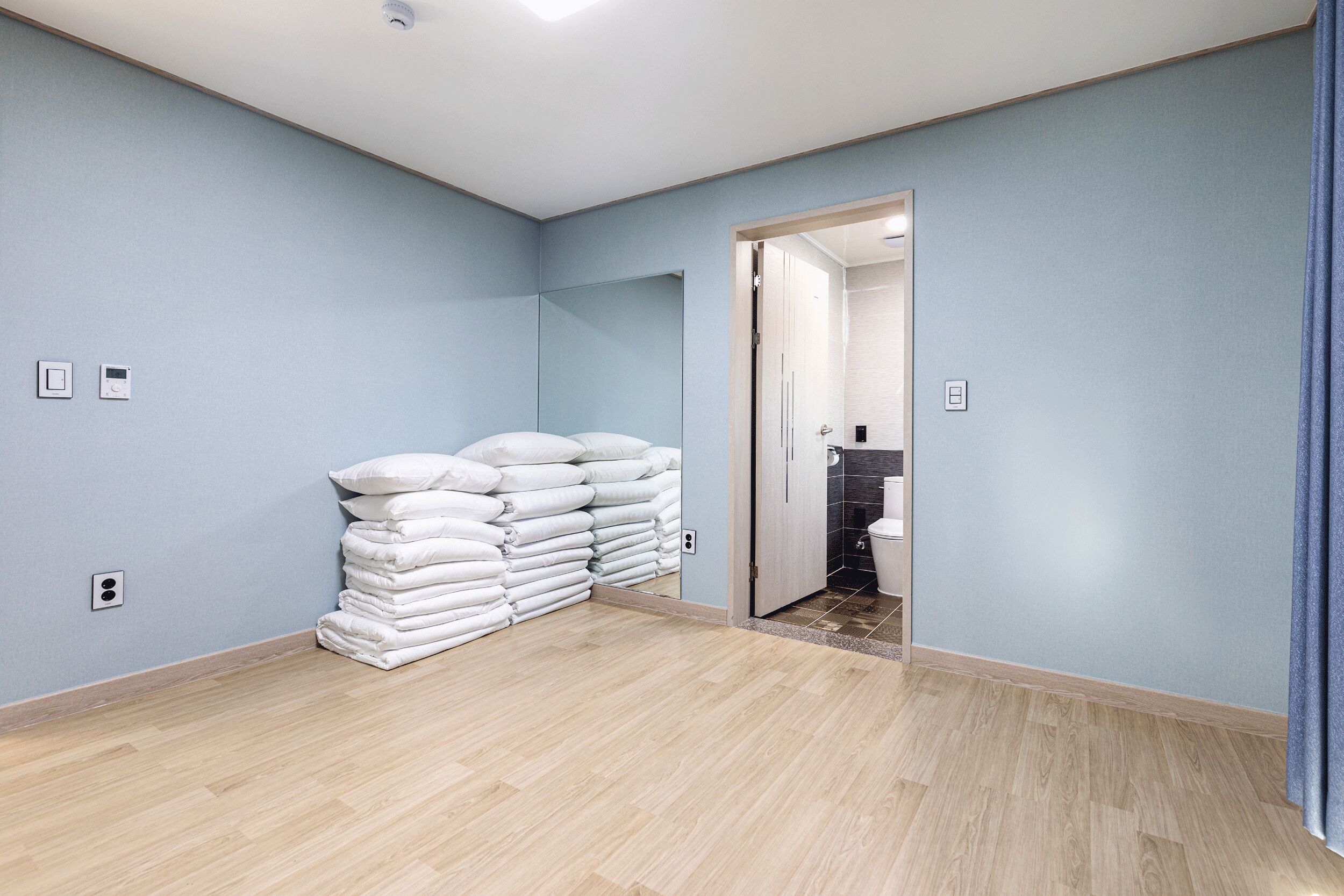 A room with light blue walls, a wooden floor, and a stack of white towels against the wall.