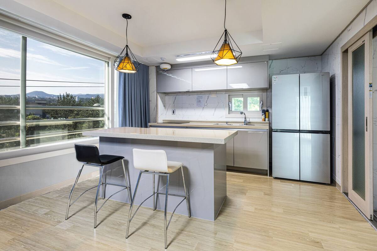 Una cocina moderna con una isla grande, taburetes de bar, un refrigerador y vistas al exterior.