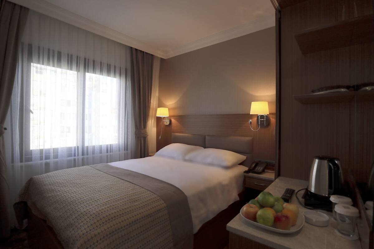 A hotel room with a large bed, two bedside lamps, a nightstand with a phone and a coffee maker, and a fruit bowl on the side table.